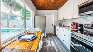A modern kitchen with white cabinets, a wooden ceiling, and a view of a swimming pool. - New listing Spacious 4-Bedroom beach cottage steps from the beach (Indian Rocks Beach)