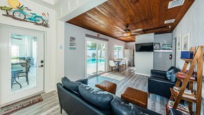 A modern living room with a wooden ceiling, a pool view, and a beach-themed sign. - New listing Spacious 4-Bedroom beach cottage steps from the beach (Indian Rocks Beach)