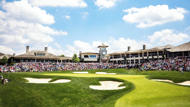 Un terrain de golf où se trouve une foule nombreuse, un beffroi et un bâtiment à plusieurs étages.