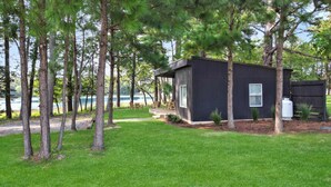 Une cabane moderne dotée d’une terrasse, entourée de grands arbres et offrant une vue sur un lac.