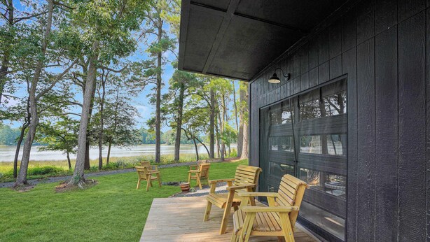 Une terrasse en bois avec des sièges extérieurs, entourée d’arbres et offrant une vue sur un lac.