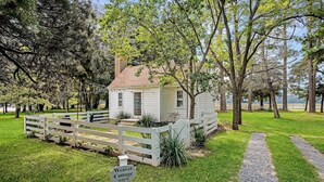 A white cottage with a white picket fence, surrounded by lush greenery and trees.