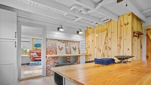 A modern kitchen with a wooden countertop, a hanging light fixture, and a brick wall with framed pictures.