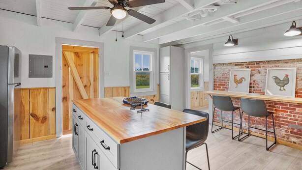 A kitchen with a wooden island, bar stools, and a ceiling fan.