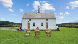 A white house with a sloped roof, a chimney, and a front porch with wooden chairs.