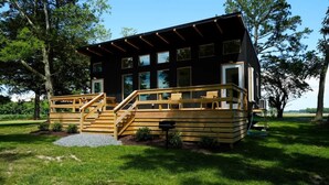 Une cabane moderne dotée d’une terrasse en bois, de nombreuses fenêtres et d’un escalier menant à l’entrée.