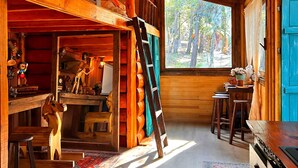 A log cabin interior with a loft bedroom, wooden furniture, and a view of the forest.