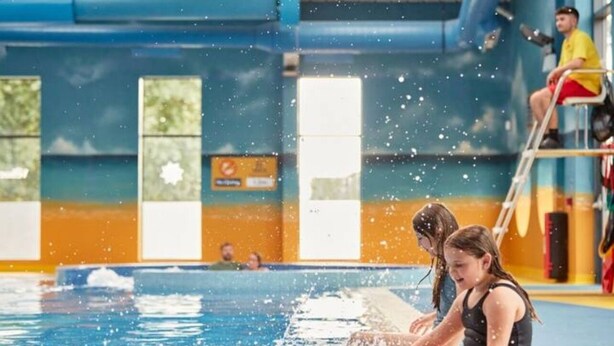 A swimming pool with two people sitting on the edge, water splashing around them. - 3 bed mobile home - Holiday Park (Northampton)