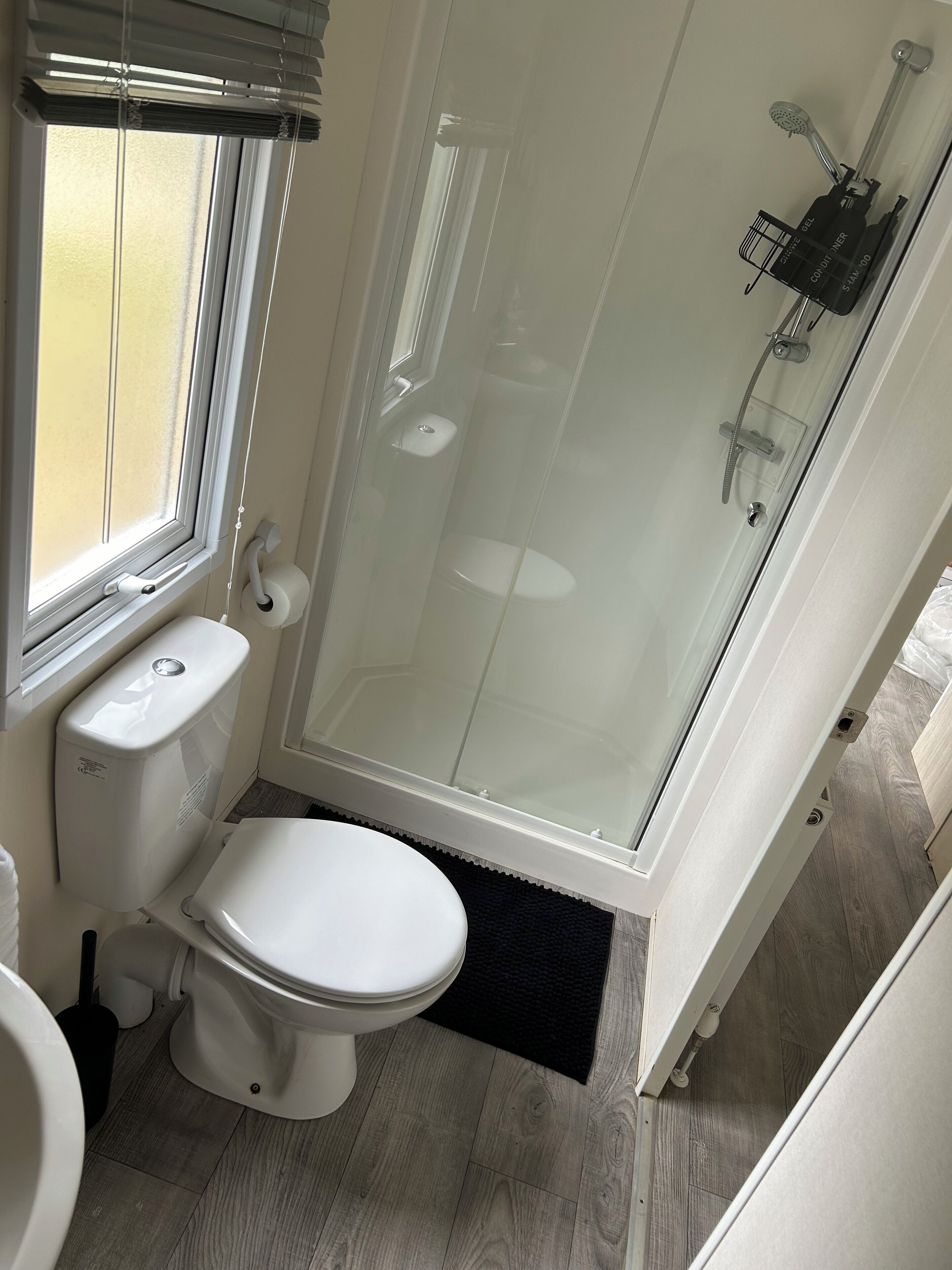 Un bagno compatto con il water, una doccia vetrata e una finestra.
