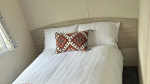 A neatly made bed with a floral bedspread and a patterned pillow. - 3 bed mobile home - Holiday Park (Northampton)