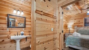 A wooden cabin interior with a bed, a sink, and a mirror. - Rustic Retreat W/ Hot Tub • Firepit - BBQ (Broken Bow)