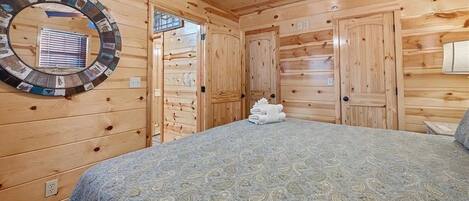 Una habitación tipo cabaña de madera con una cama, un espejo circular y un ventilador de techo.