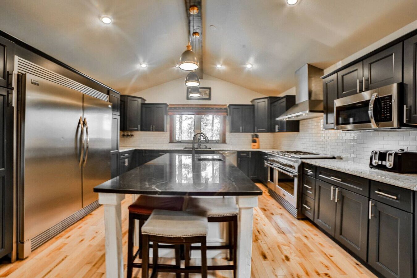 A modern kitchen with a central island, stainless steel appliances, and dark cabinetry.