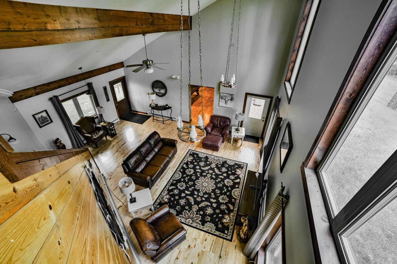 A spacious living area with a high ceiling, wooden beams, a large window, and a fireplace.