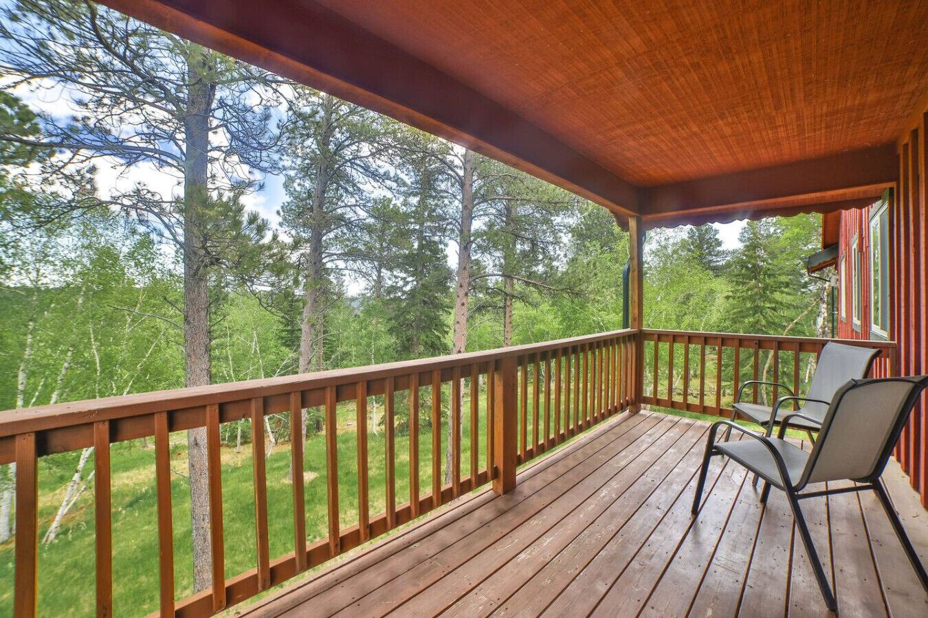 A wooden deck with a railing, two chairs, and a view of a forest.