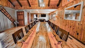 Een grote houten eettafel met stoelen, omringd door houten wanden en een schuin dak.