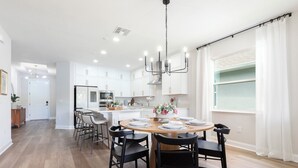 A modern kitchen with white cabinets, a central island, and a dining area with a round table and chairs. - Stylish waterside retreat - springs nearby - pool and gym access - large groups (DeBary)
