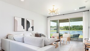A modern living room with a white sofa, a coffee table, and a view of a lake through large glass doors. - Stylish waterside retreat - springs nearby - pool and gym access - large groups (DeBary)
