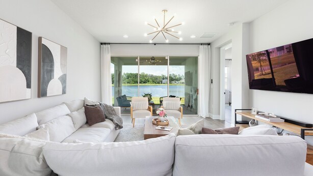 A modern living room with a white sofa, a coffee table, and a TV on the wall. There is a large window with a view of greenery and a pool. - Stylish waterside retreat - springs nearby - pool and gym access - large groups (DeBary)