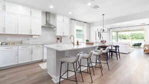 A modern kitchen with white cabinetry, a large island, and bar stools. - Stylish waterside retreat - springs nearby - pool and gym access - large groups (DeBary)
