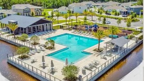 A swimming pool with lounge chairs and umbrellas, surrounded by a fence and palm trees. - Stylish waterside retreat - springs nearby - pool and gym access - large groups (DeBary)