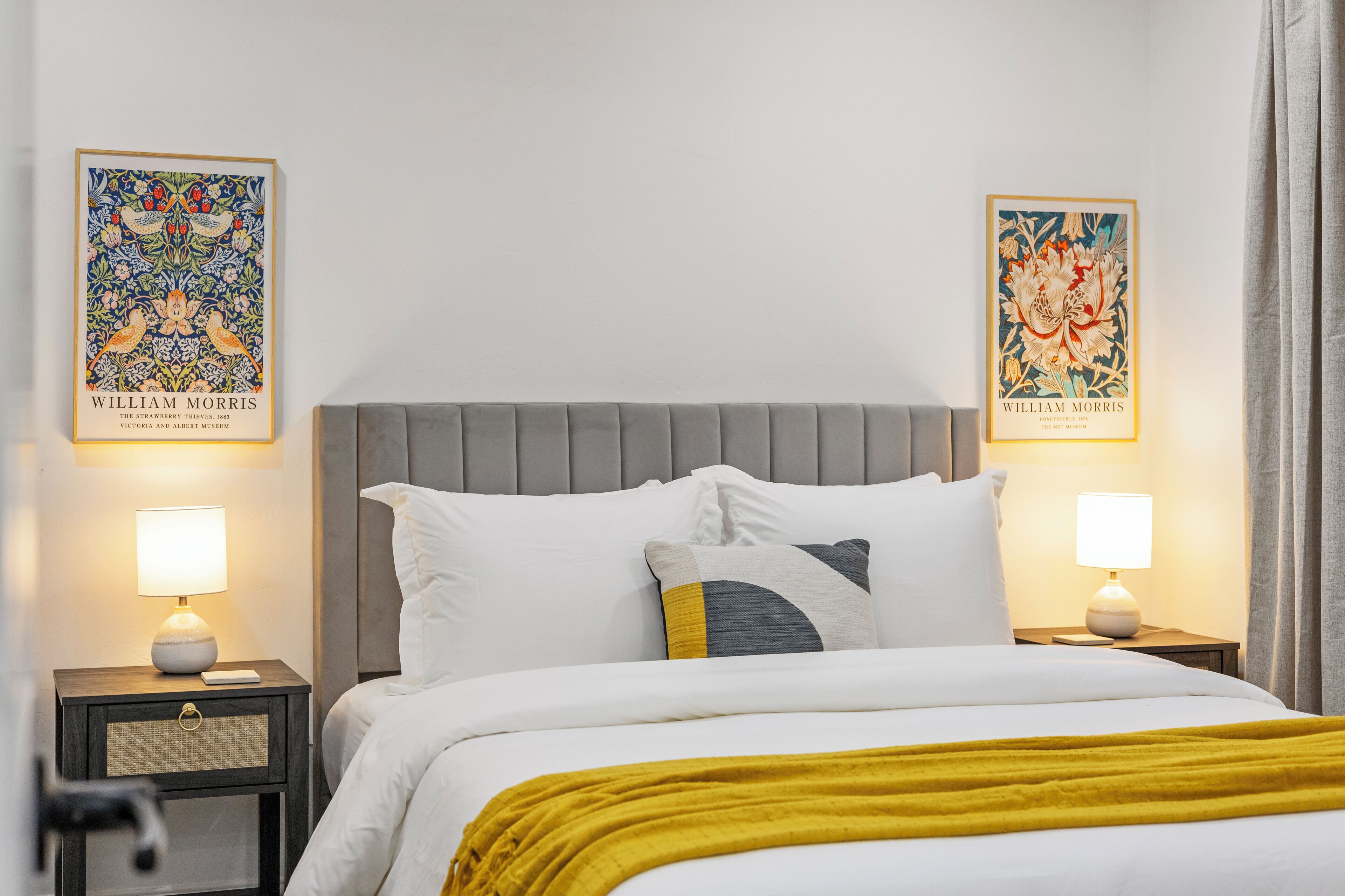 A hotel room with a bed, two nightstands, two lamps, and two framed artworks on the walls.