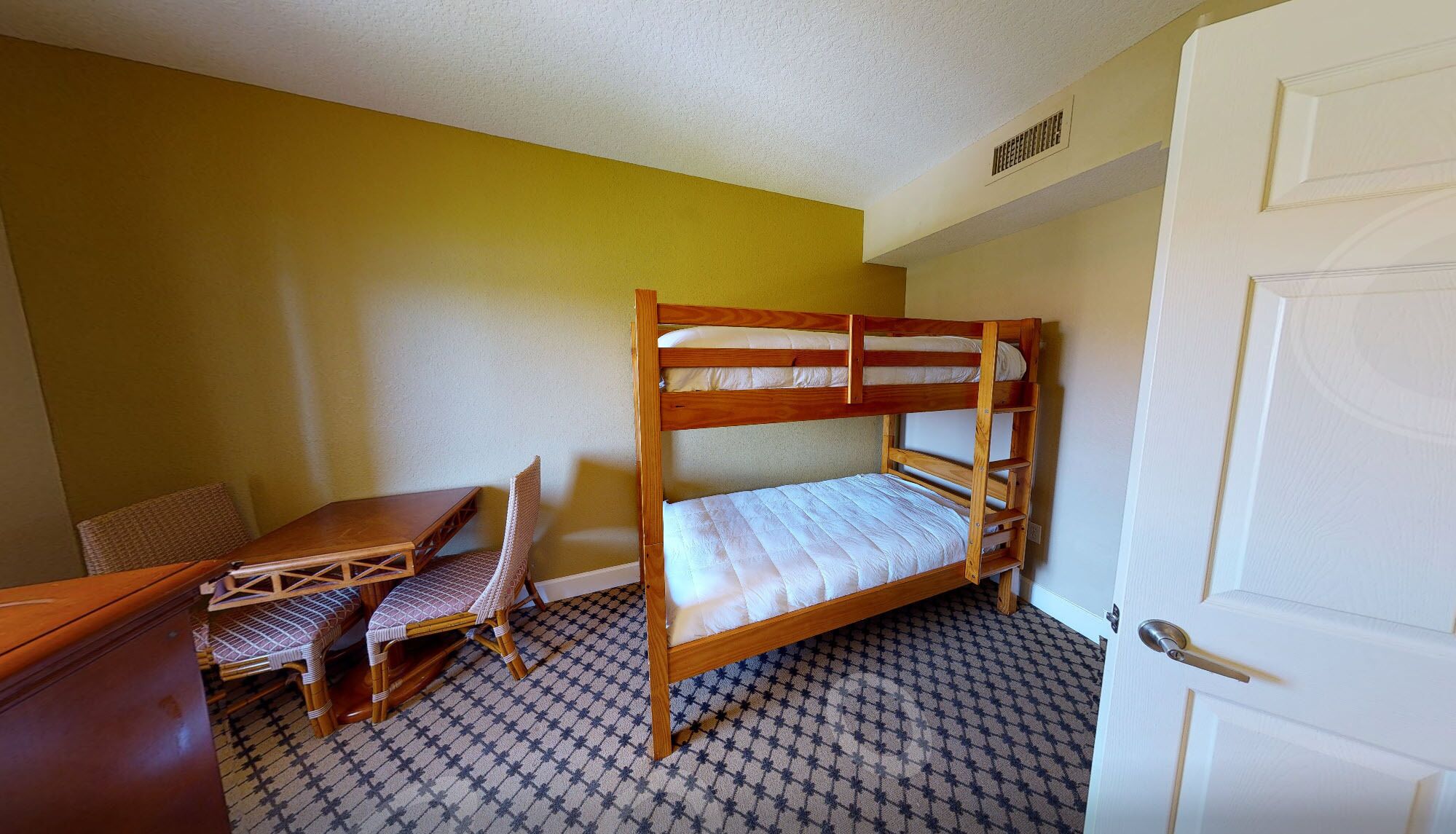Quarto com beliches, escrivaninha de madeira e cadeiras de vime.