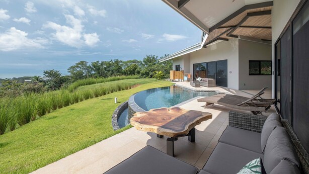 A modern outdoor pool area with a wooden table, lounge chairs, and a view of the surrounding landscape. - Stunning Ocean View Home on Nature Reserve (Esterillos Este)