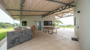 A modern kitchen with a stone island, wooden ceiling, and a large window overlooking a green landscape. - Stunning Ocean View Home on Nature Reserve (Esterillos Este)