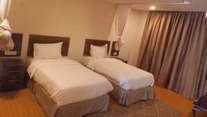A hotel room with two beds, a nightstand, a lamp, and a curtain.