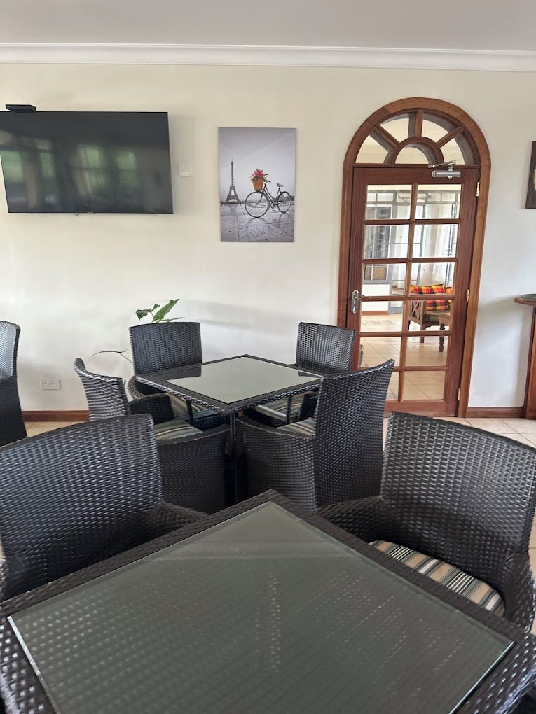 A dining area with a glass-top table surrounded by wicker chairs, a television mounted on the wall, and a door leading to an outdoor space.
