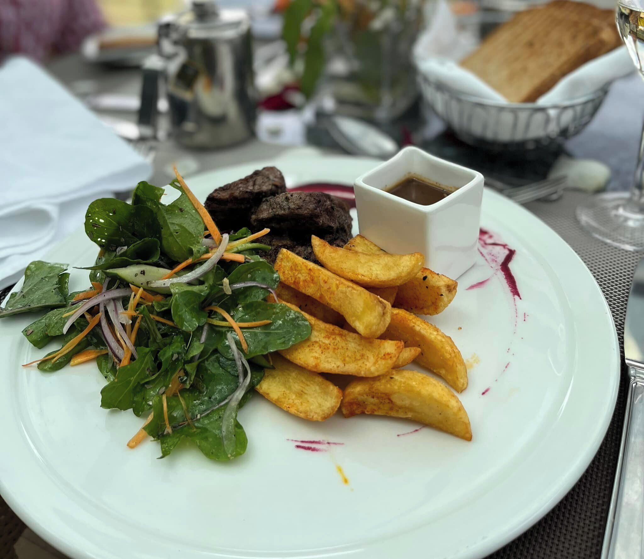 A plate with a salad, fries, and a small bowl of sauce.