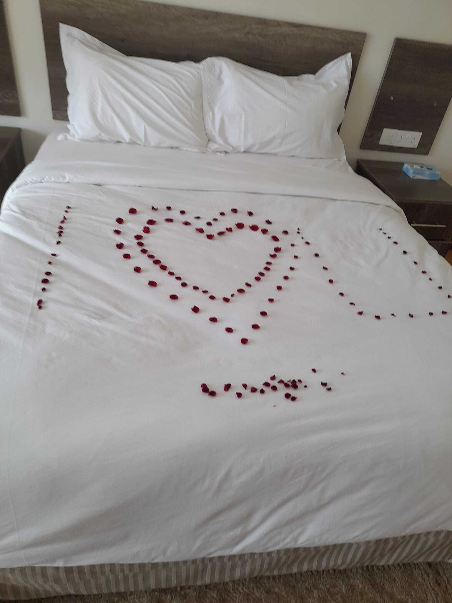 A neatly made bed with a heart-shaped decoration made of rose petals on the bedspread.