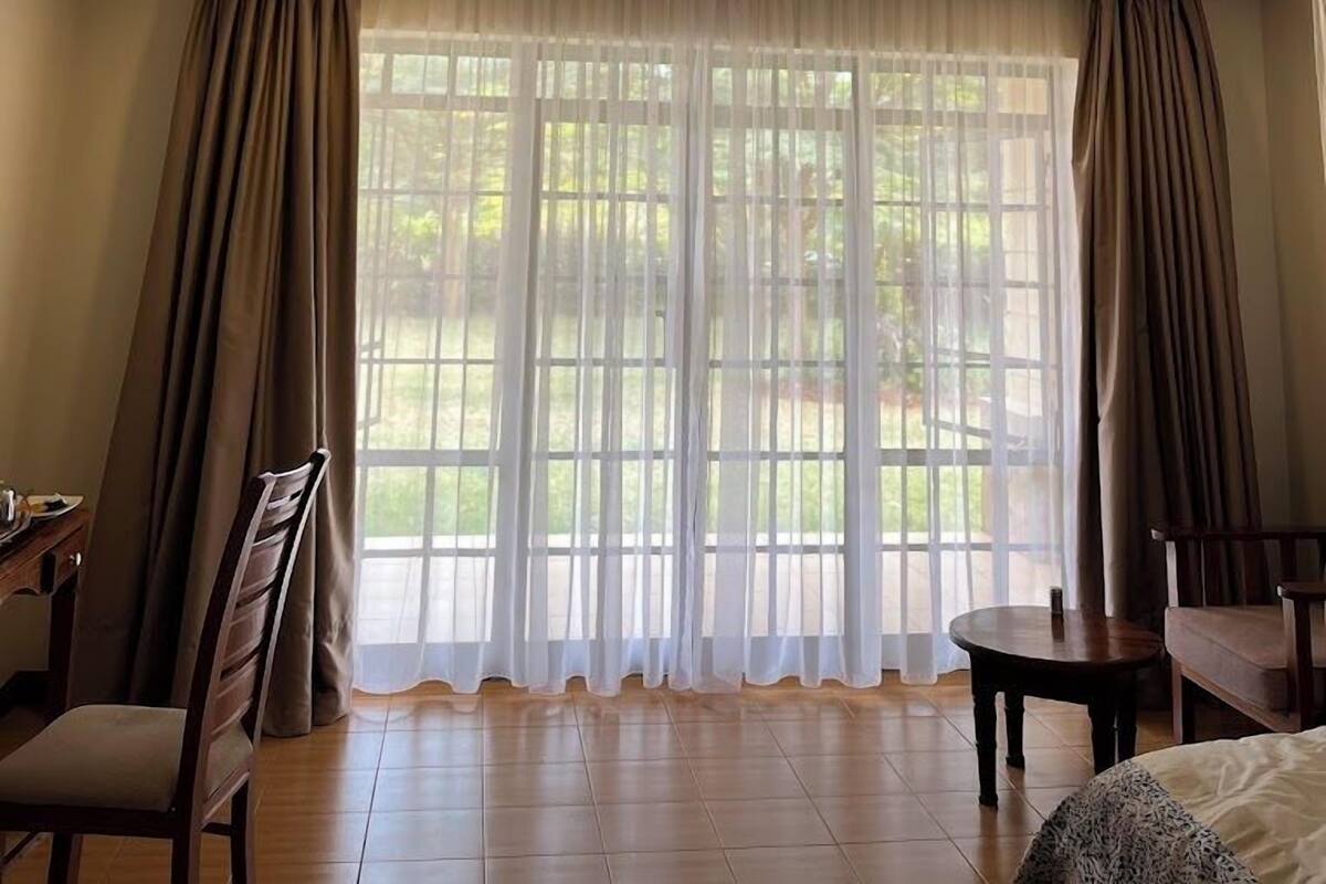 A hotel room with a large window, a bed, a chair, and a small table.
