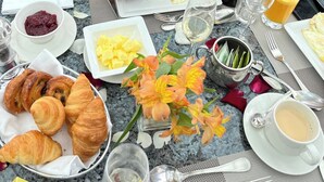 A breakfast setting with croissants, fruit, flowers, and coffee on a marble table.