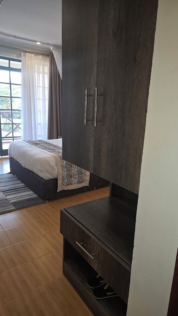 A bedroom with a large bed, a wardrobe with two handles, a small shelf, and a window with curtains.
