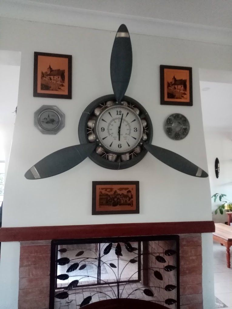 A wall-mounted clock with a unique design, surrounded by framed pictures and decorative plates.