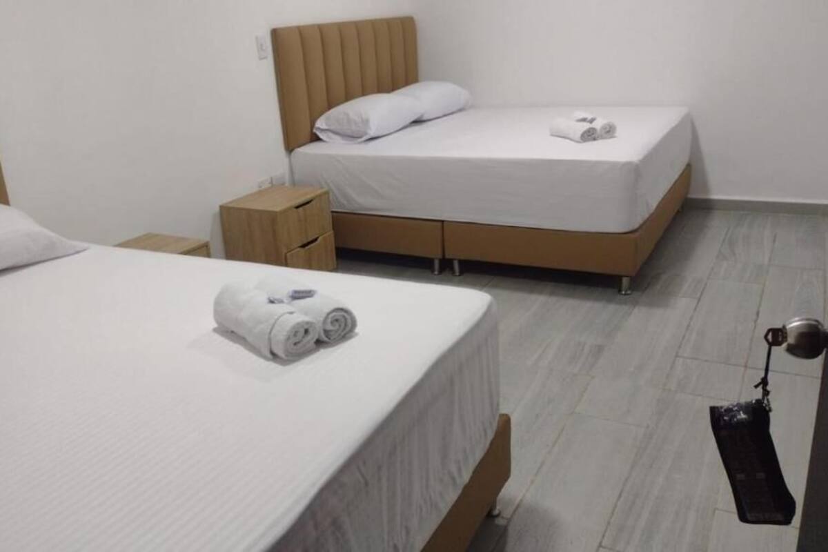 A hotel room with two beds, a wooden nightstand, and a door with a towel rack.