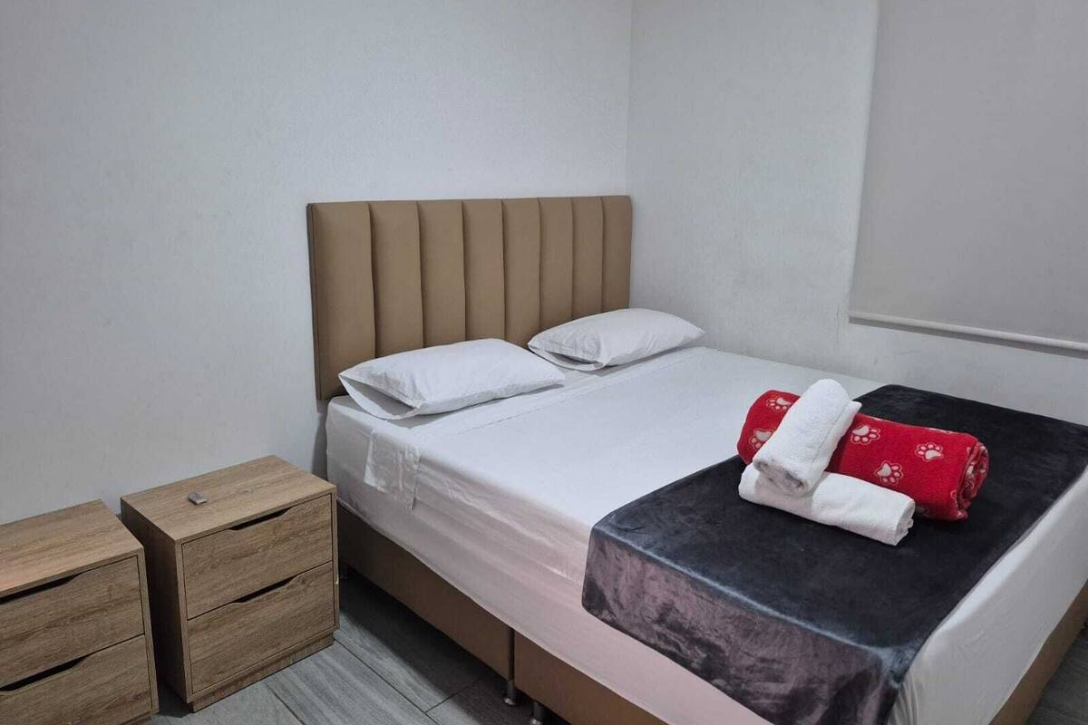 A single bed with a headboard, a wooden nightstand with drawers, and a window with a blind.