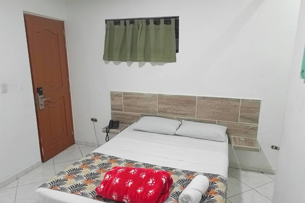 A bedroom with a bed, a telephone, a door, and a window with curtains.