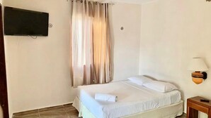 Un dormitorio con cama, televisor montado en la pared, lámpara y cortina.