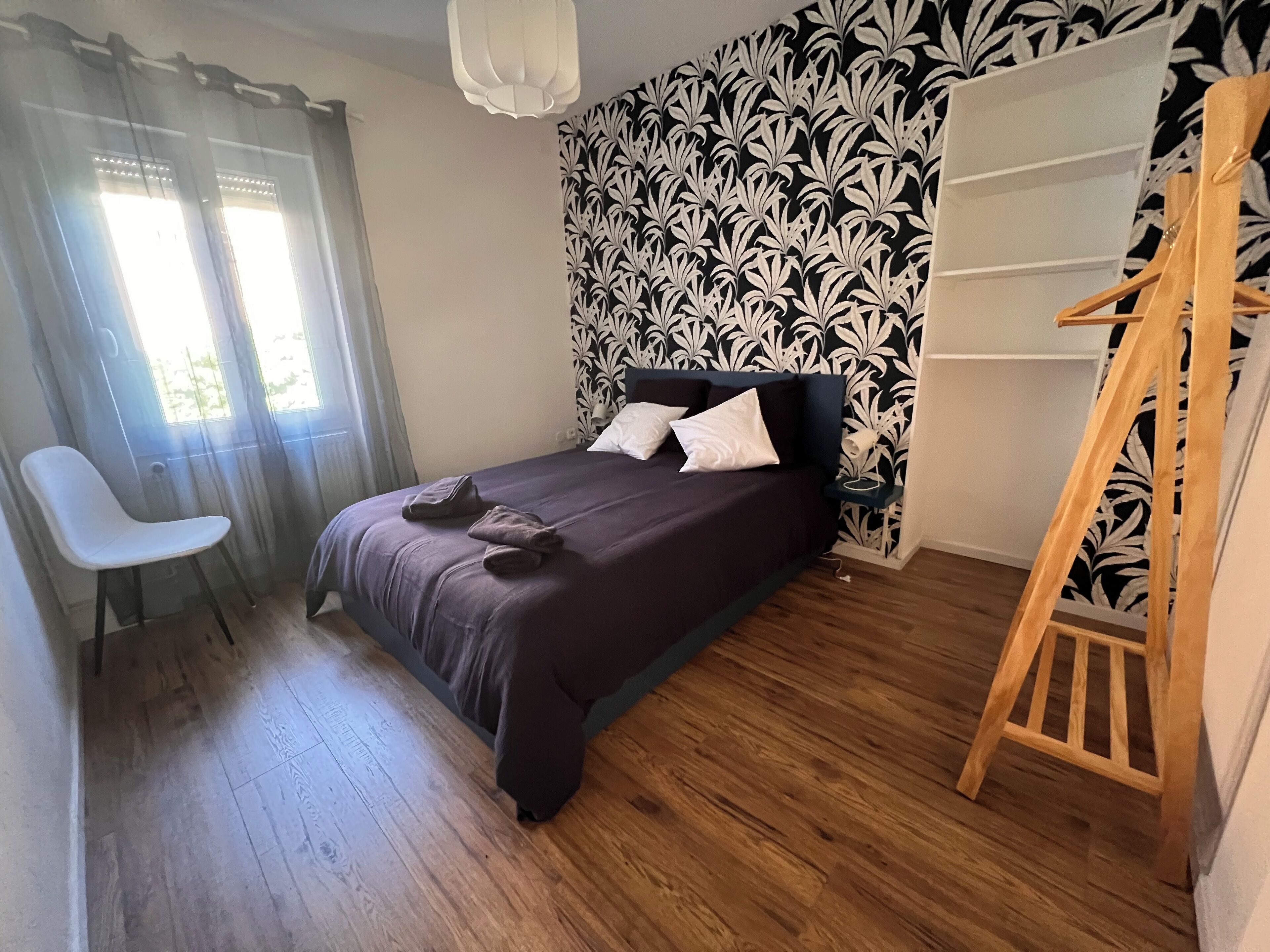 Una camera da letto con un letto, una sedia, una scala in legno e una parete decorata.