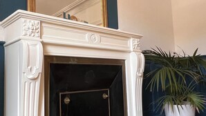 A white fireplace with a black door, a large mirror above it, and a potted plant to the right. - Apartment in the heart of Le Creusot (Le Creusot)