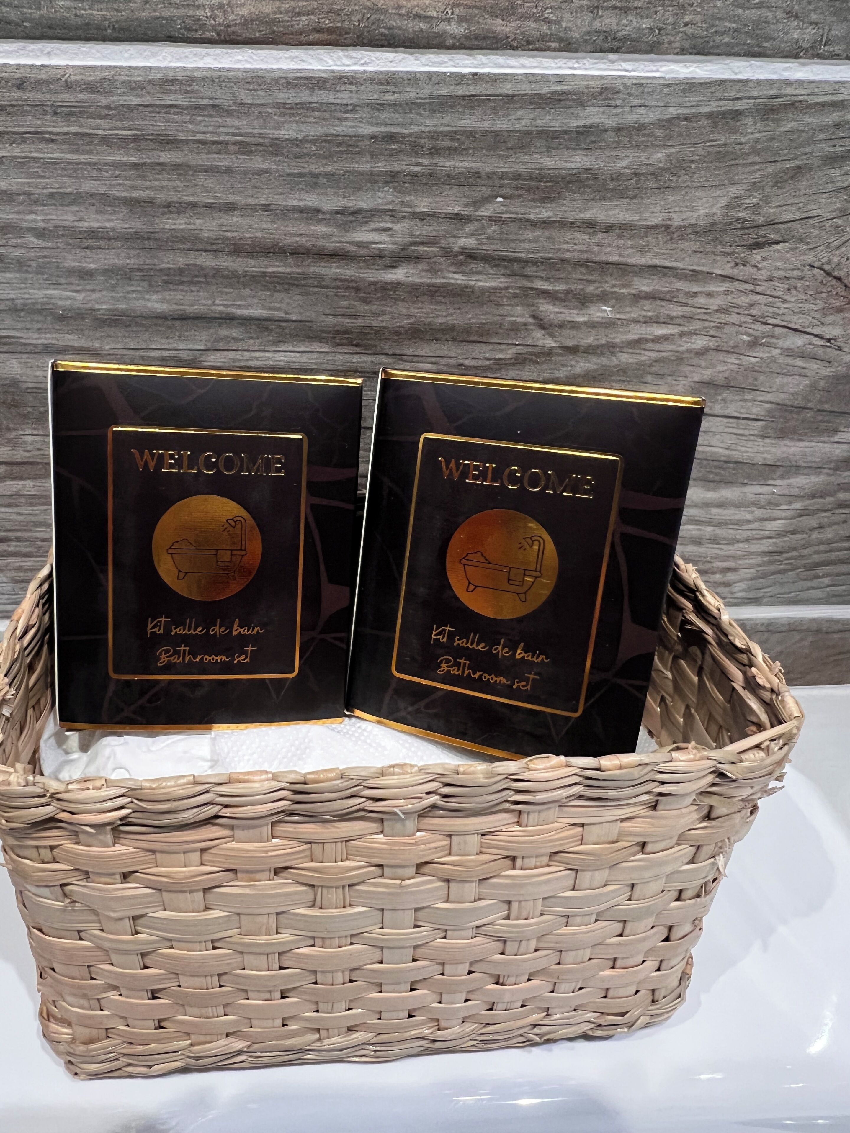 Deux panneaux d’accueil noirs, avec des lettres dorées et un emblème circulaire, disposés dans un panier tressé.