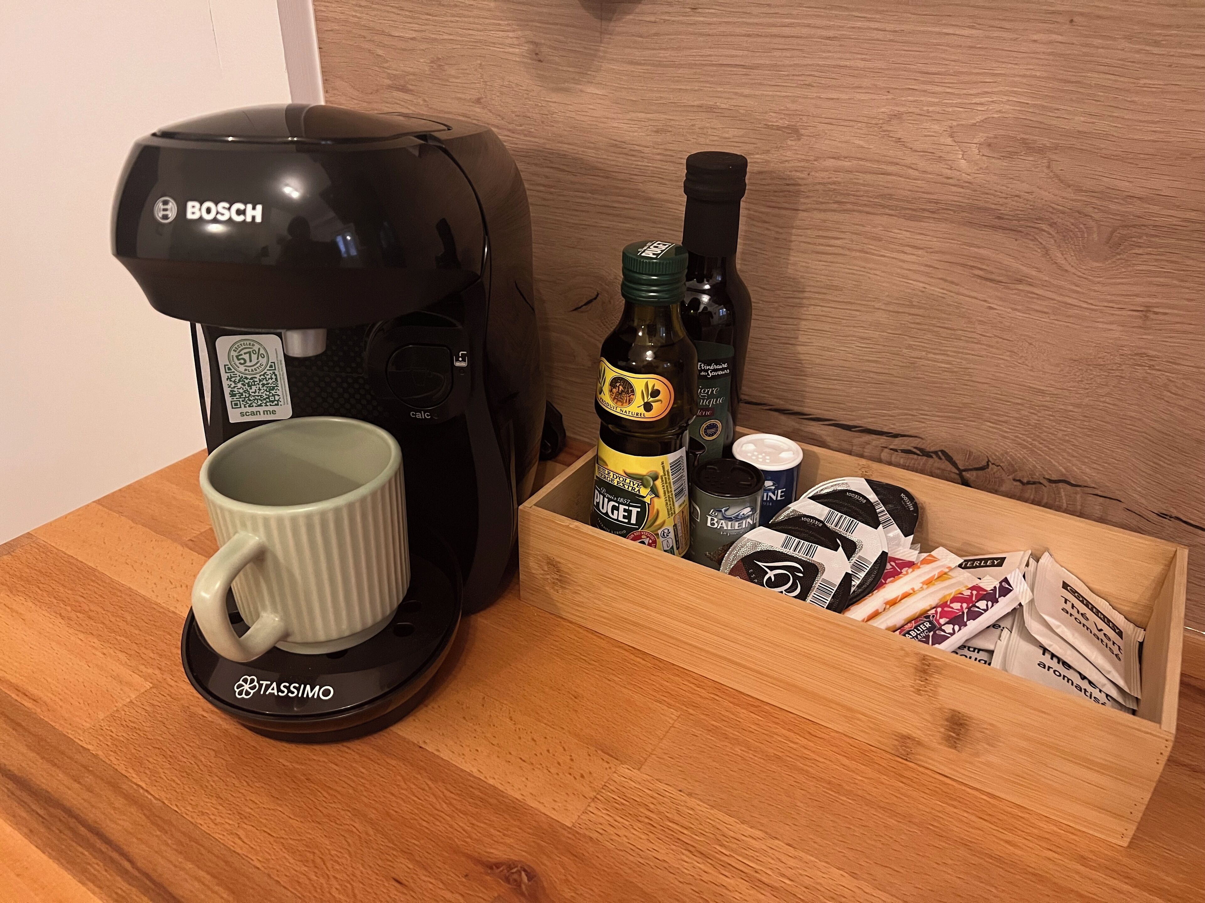 Eine Kaffeemaschine, eine Tasse und eine Schublade mit verschiedenen Gegenständen, darunter Flaschen und Beuteln.
