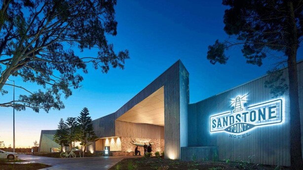 A modern hotel with a prominent 'SANDSTONE POINT' sign, large windows, and a well-lit entrance area.