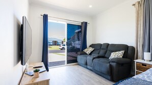 A modern hotel room with a sofa, a TV, a desk with a laptop, and a view of the outside.