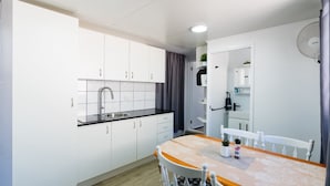 A compact kitchen with white cabinets, a black countertop, and a sink. There is a dining table with chairs and a small potted plant.