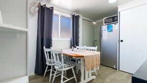 A compact kitchen with a dining table, chairs, a refrigerator, and a window with curtains.