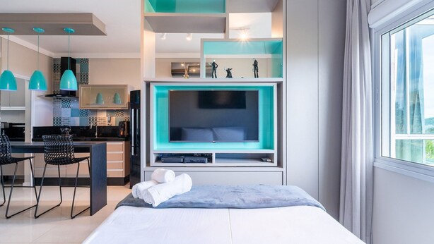 Ein modernes Hotelzimmer mit einem großen Bett, einem Fernseher, einem Schreibtisch mit Stühlen und einer Küchenzeile.